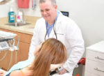 A general dentist smiling at a woman in a dentist's chair.